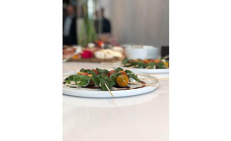 Tomato, mozzarella, and basil hors-d'oeuvres drizzled with balsamic vinegar displayed on white ceramic serving dishes