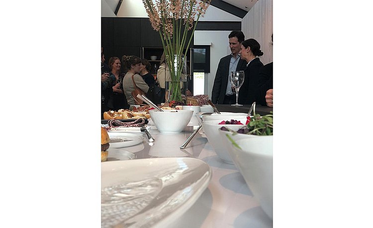 View of serving dishes filled with delicious hors-d'oeuvres with guests gathering and having conversations in the background
