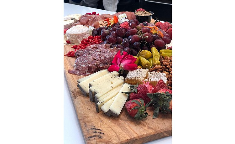 Beautiful display of wooden cutting board filled with a variety of delicious cheese, meat, and fruit