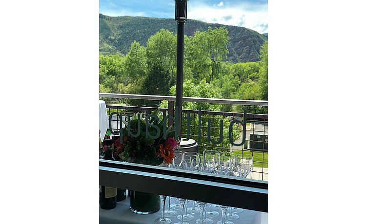 bulthaup logo on window looking outside to the balcony filled with linen draped high top tables and bar area looking out over mountain range