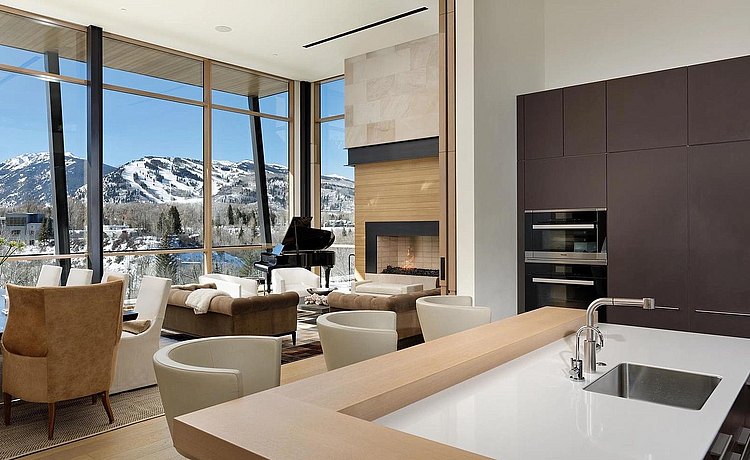 Partial view of living space and kitchen space including bar top finished in natural oak. Tall elevation where appliances are located finished in soft touch lacquer. Countertop is white quartz. A beautiful backdrop of the Aspen mountain range. 